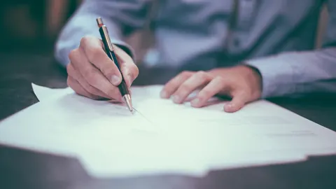 Hand, die ein ausgedrucktes Blatt mit einem Stift unterschreibt
