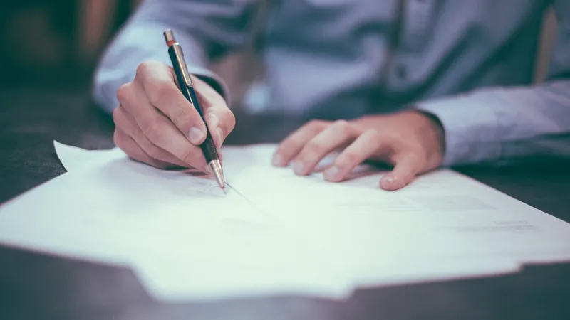 Hand, die ein ausgedrucktes Blatt mit einem Stift unterschreibt