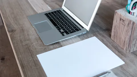 Weißes Blatt Papier neben einem Laptop auf einem Holzschreibtisch