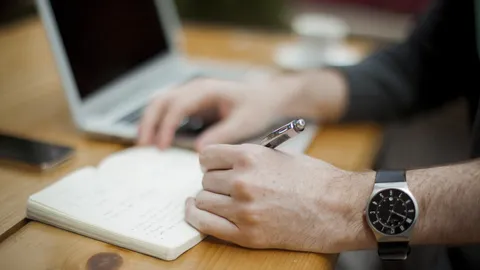 Hand, die mit einem Stift Notizen in ein Heft schreibt